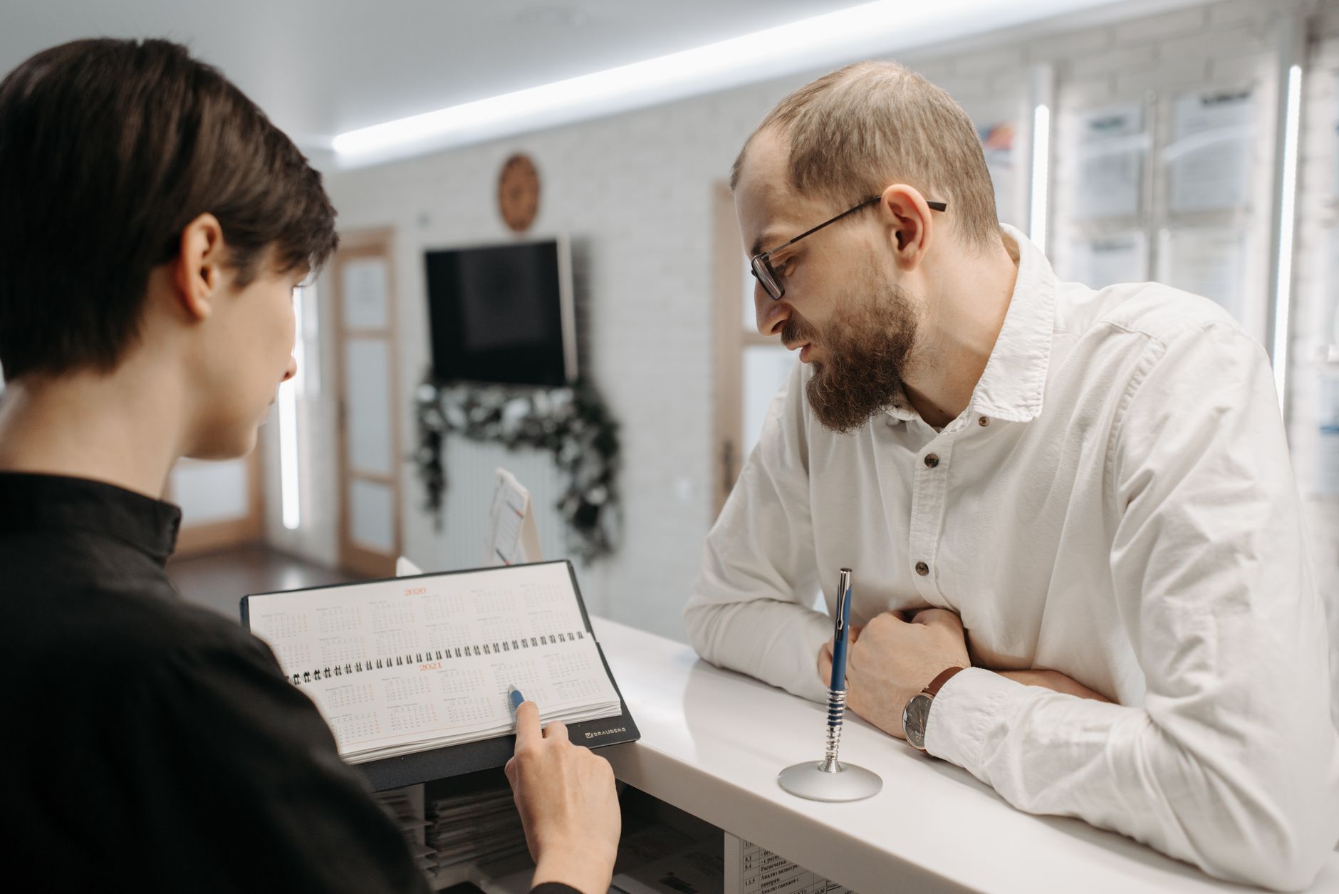Recepcionista anotando em uma agenda de papel enquanto atende um paciente no balcão da clínica